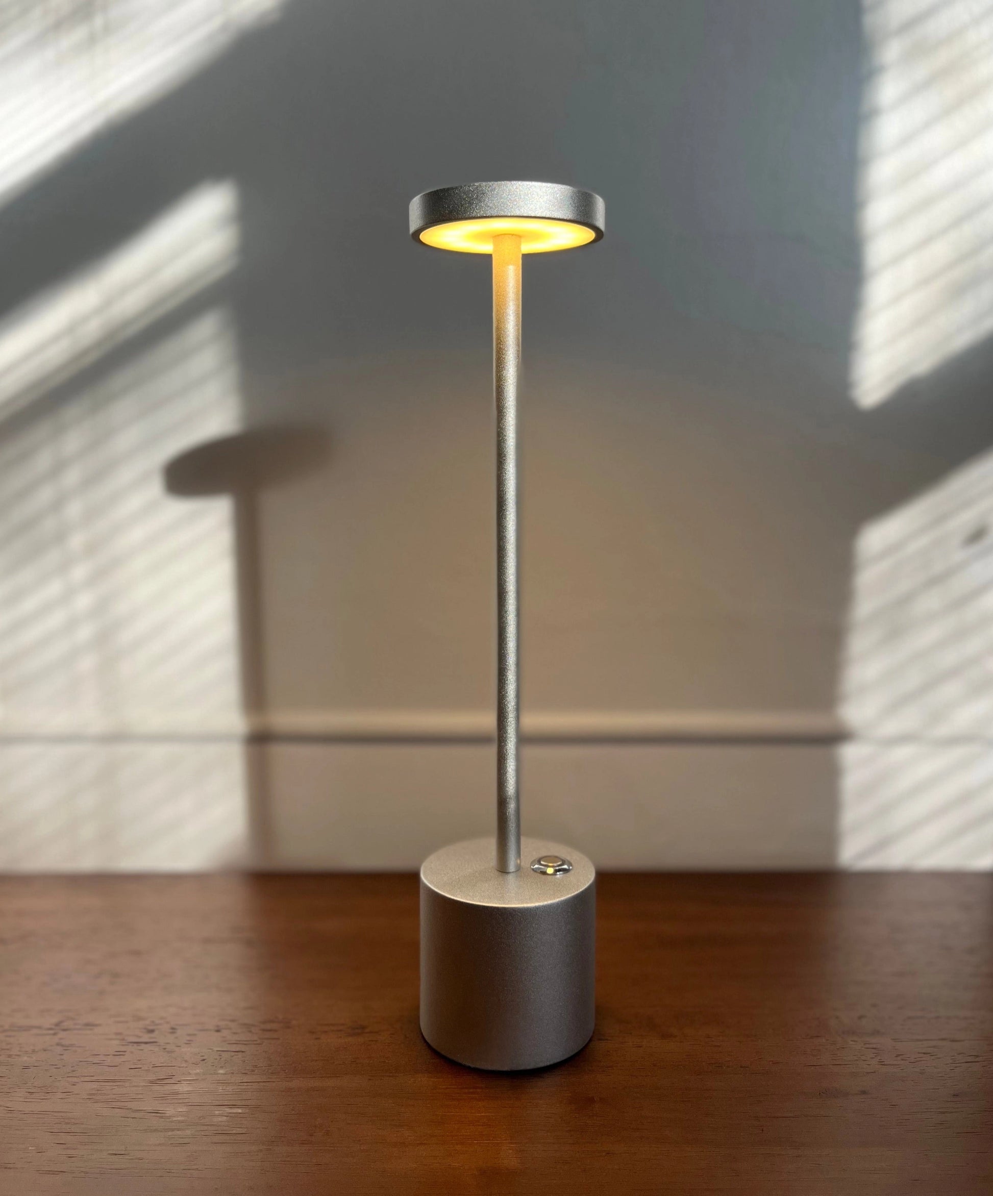 LED Portable Table Lamp with Resilient Design on a wooden surface, featuring a circular base with metal and glass elements.