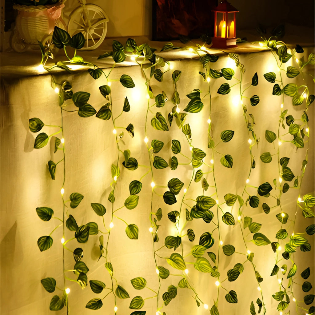 LED Vine Garden String Lights with Ivy Vines featuring 100 LEDs and watermelon leaves, 32ft long, illuminating a wall with a warm, green glow.
