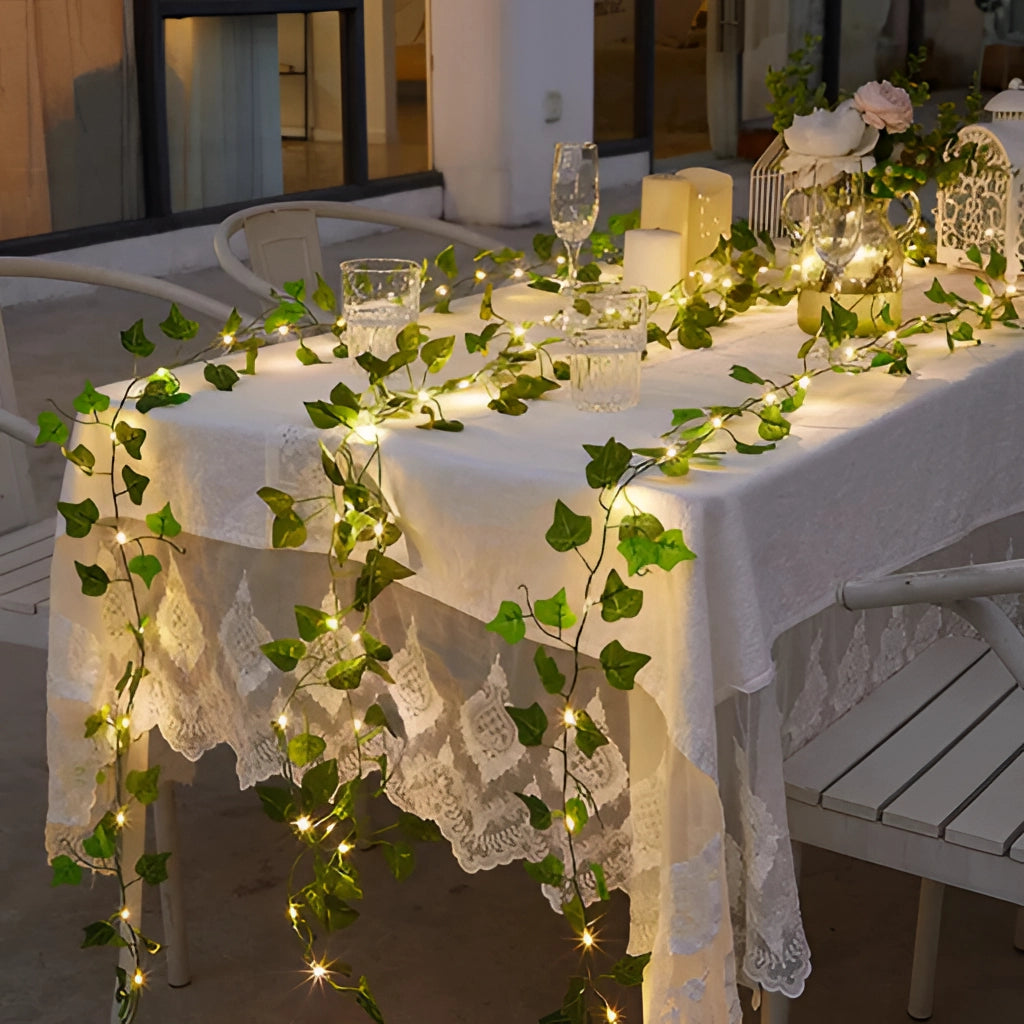 LED vine garden string lights with ivy vines, 32ft with 100 LEDs, draped over a table set with tableware and a tablecloth, enhancing interior design with decorative lighting and plant elements.