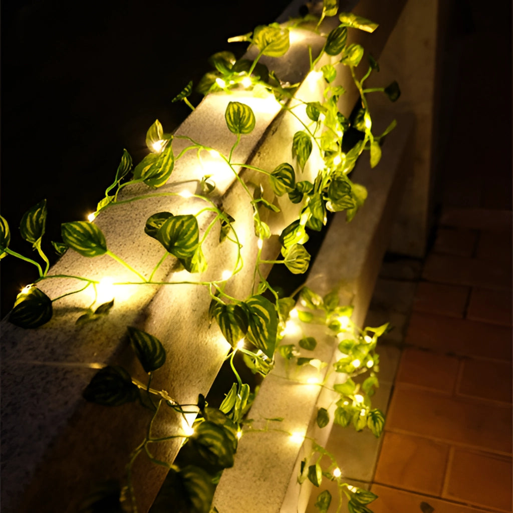 LED vine garden string lights with ivy vines, 32ft 100 LEDs, decorated with realistic green leaves and white flowers, draped on a ceiling for an event.