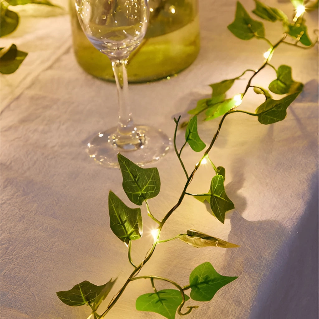 LED Vine Garden String Lights with Ivy Vines - 32ft 100 LEDs draped around a table setting with wine glasses and green plants.