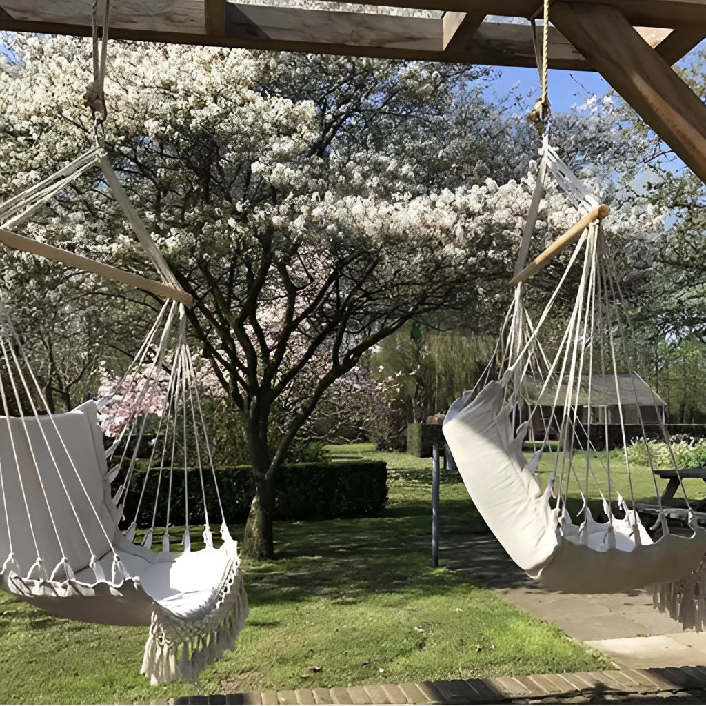 Macramé hammock swing hanging from a tree in a garden, surrounded by grass and plants, with a clear sky in the background.
