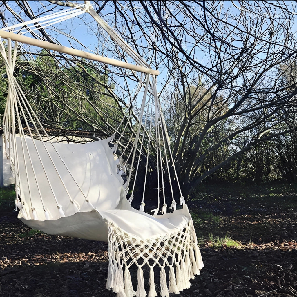 Macramé hammock swing hanging in a garden surrounded by trees and greenery with a clear sky in the background.