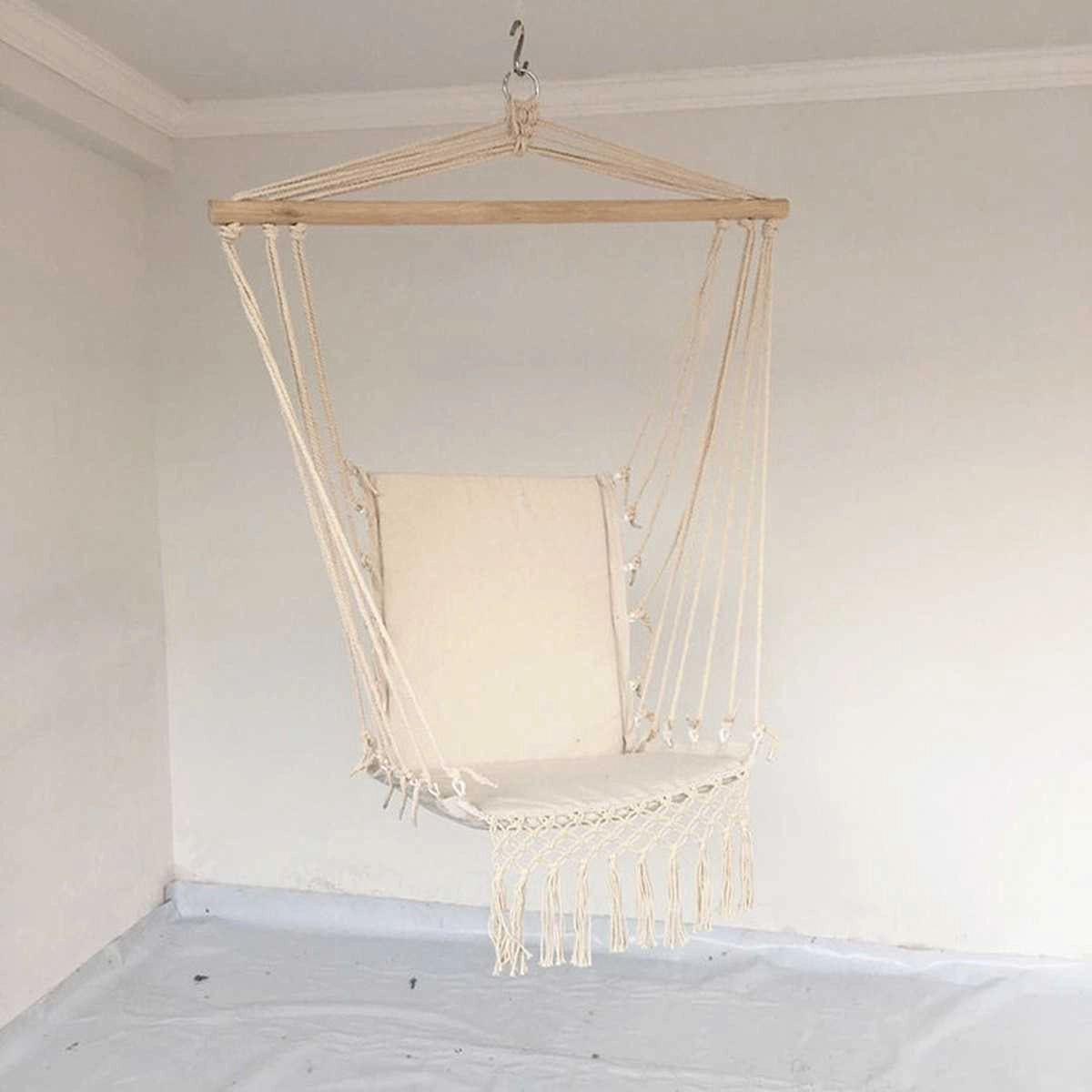 A macramé hammock swing made of natural materials hanging from a wooden ceiling fixture in a garden.