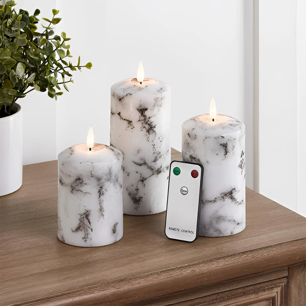 A trio set of marble LED flameless candles placed on a wooden surface with a houseplant and flowerpot nearby.
