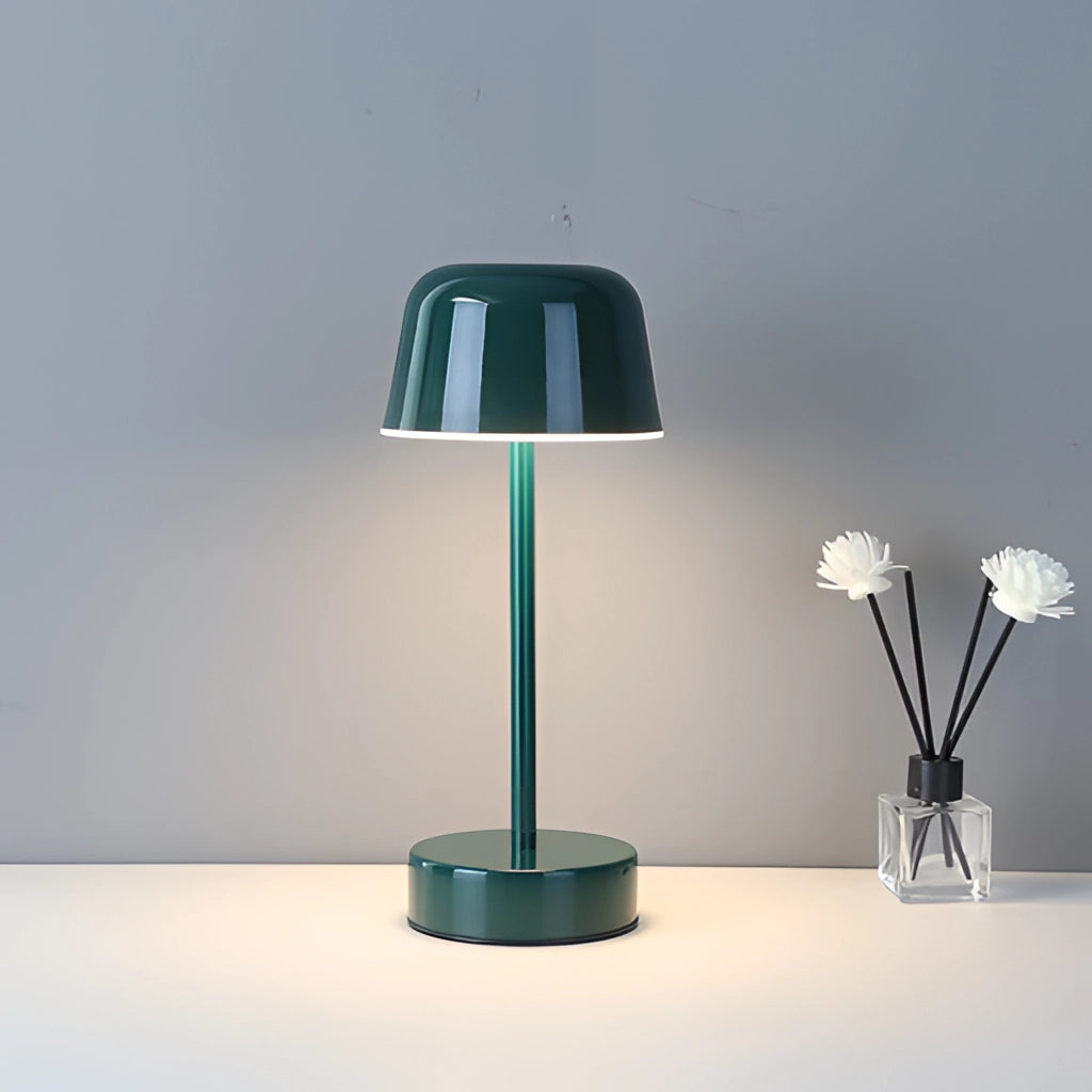 Green metal table lamp with adjustable brightness, sitting on a table next to a vase with flowers.