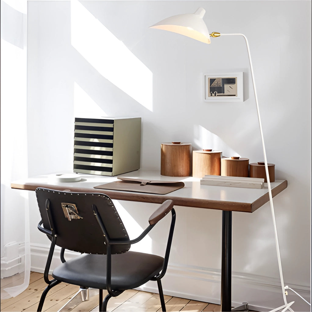 Midcentury floor lamp with tilting heads in white next to a wooden table and chair in a modern bedroom setting.