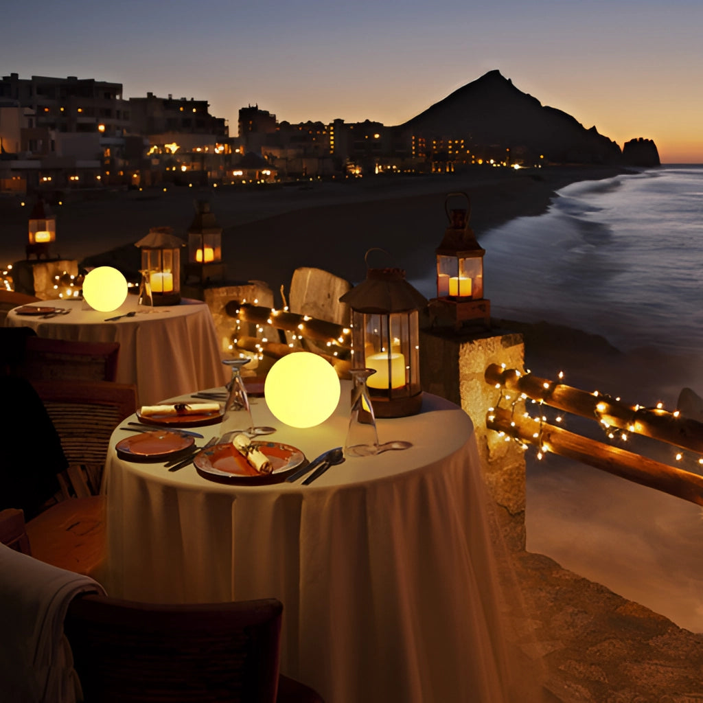 Moon Cordless LED Table Lamp with Color Control placed on a modern table indoors, surrounded by furniture and tableware, with a view of sky and buildings in the background.