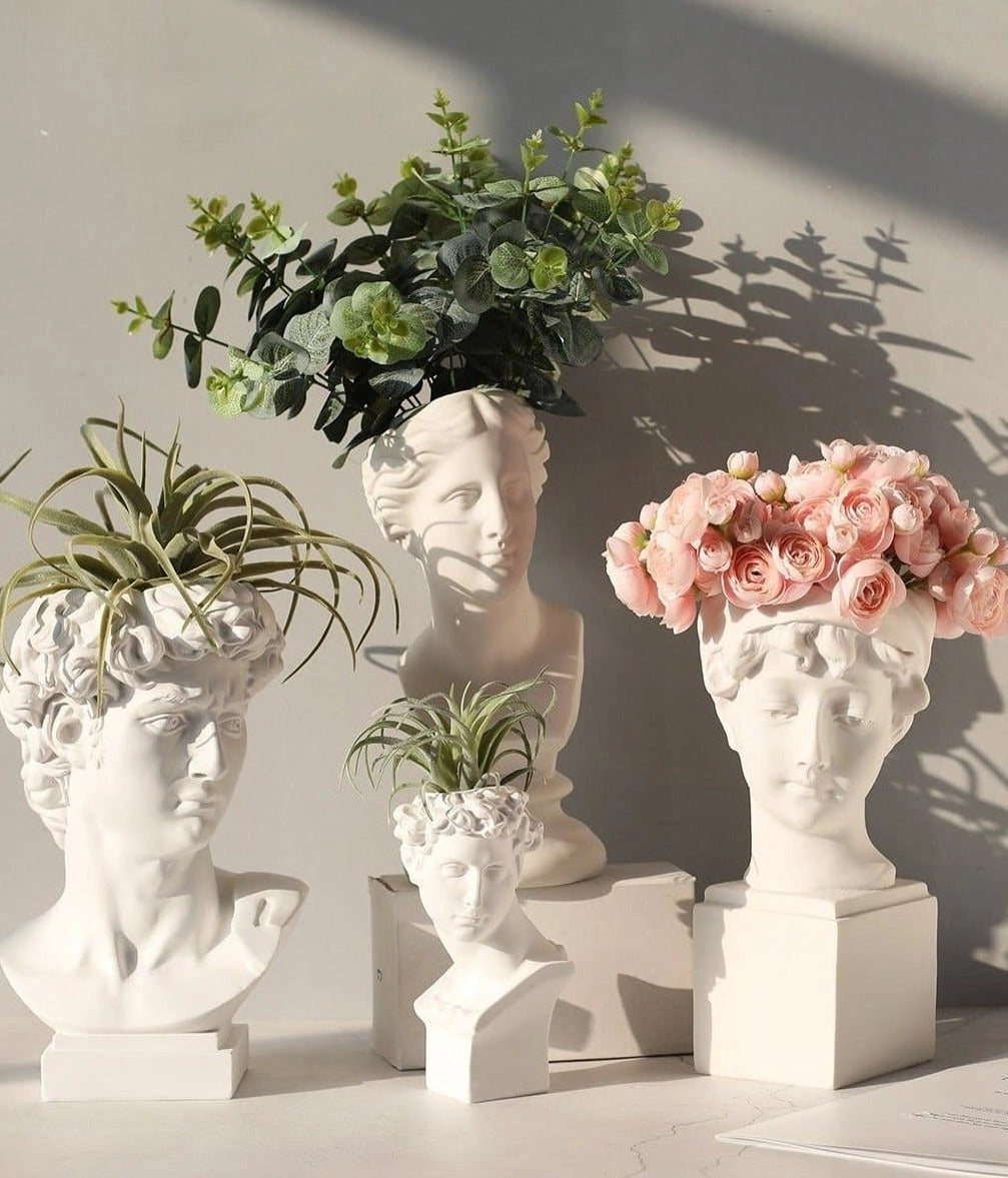 Neoclassical Greek head resin vase planter with houseplant and flowers, used as a decorative artifact in interior design.