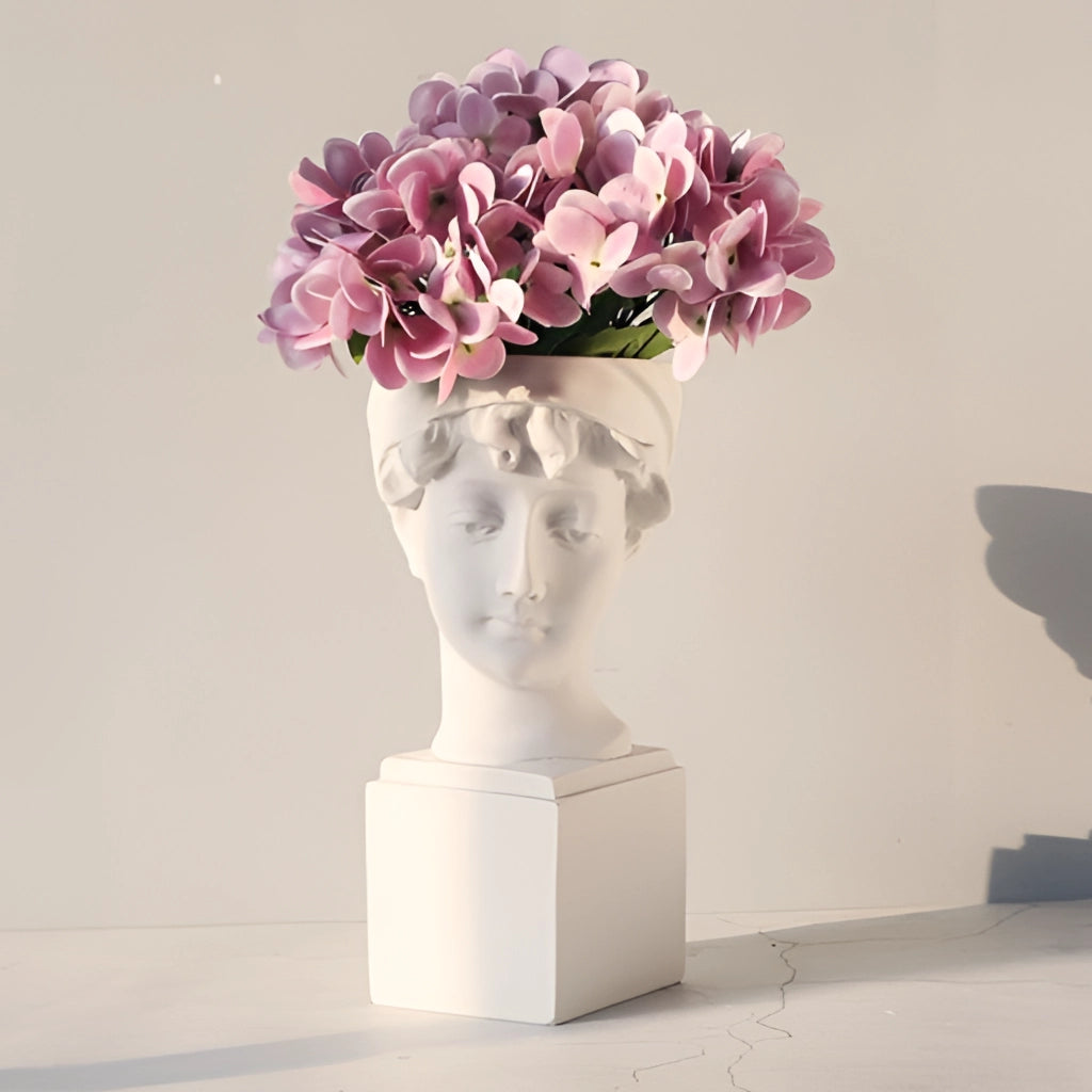 Neoclassical Greek head resin vase with a bouquet of artificial flowers and houseplants.