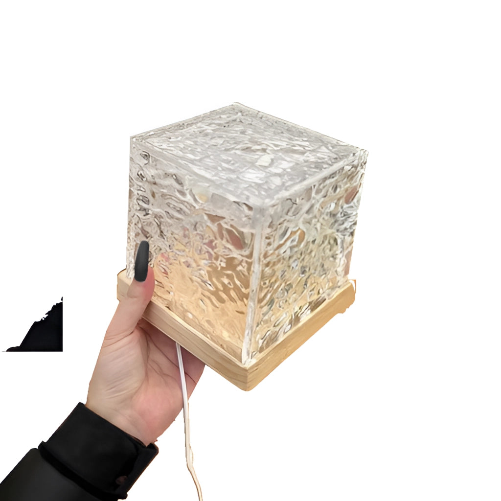 A cube-shaped lamp with Northern Lights-inspired colors, featuring a wooden frame and metal accents. It is placed in a room setting.
