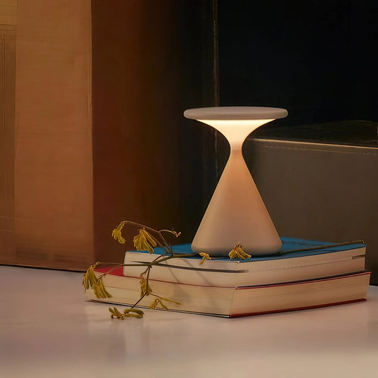 Outdoor cordless lamp emitting a soft glow, placed on a rectangular wooden table adorned with elegant serveware and drinkware, creating a sophisticated ambiance.