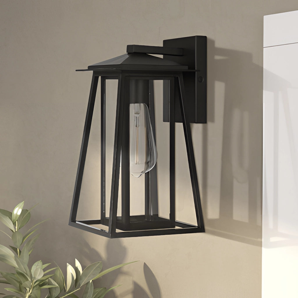 Outdoor wall lantern sconce with black steel frame and glass panels, mounted on a wooden wall, with green plants in the background.