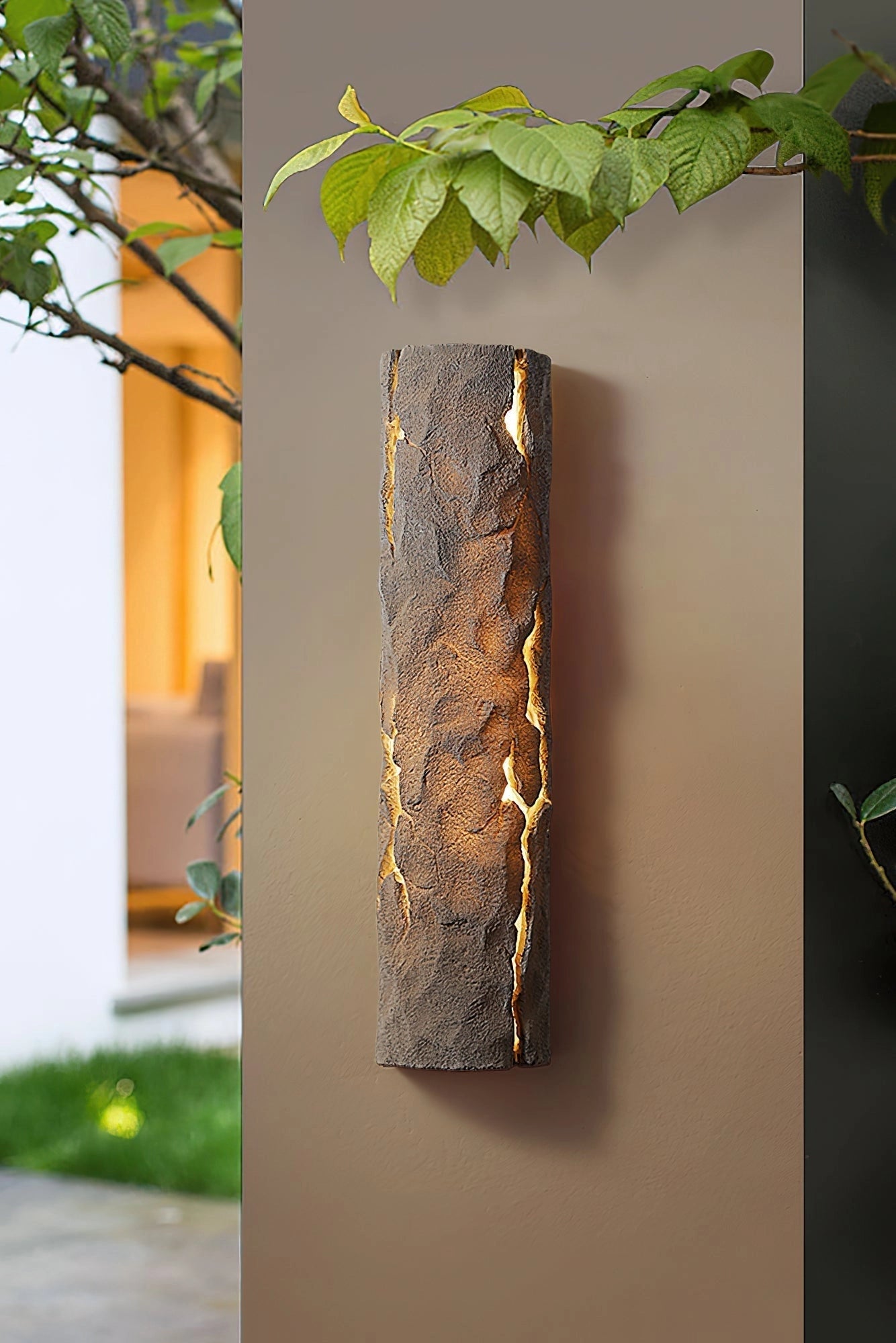 Outdoor wall light with IP65 waterproof rating in premium resin faux rock finish, surrounded by plants and branches.