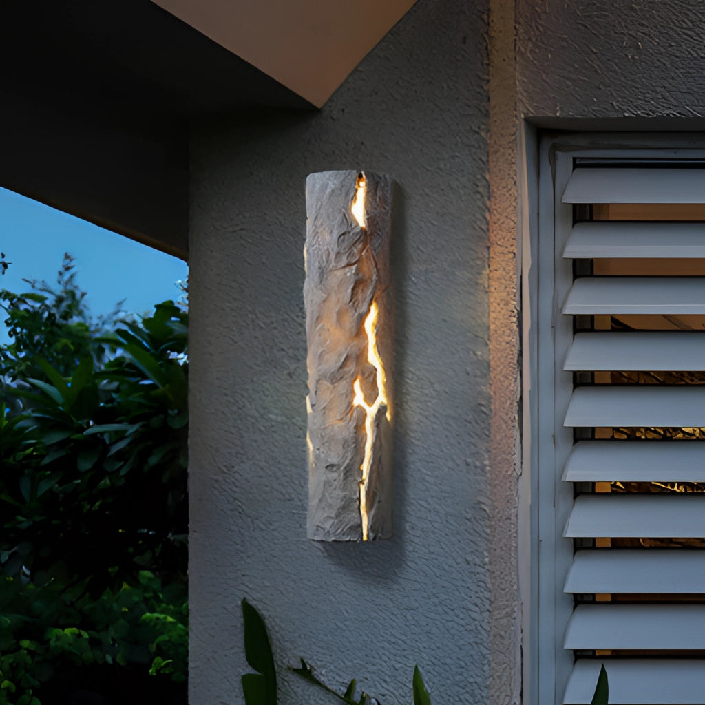 Outdoor wall light with IP65 waterproof rating and premium resin faux rock finish, mounted on an exterior house wall near a window, surrounded by plants.