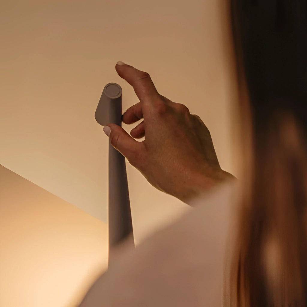 Portable rechargeable LED table lamp with aluminum construction and three light intensities, shown on a wooden surface with a hand gesturing near it.