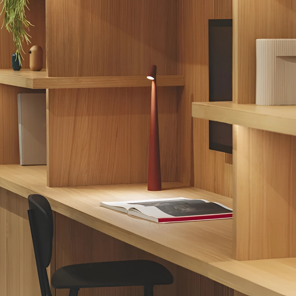 Portable rechargeable LED table lamp made of aluminum with three light intensities, placed on a wooden table next to a houseplant, enhancing the interior design of the room.
