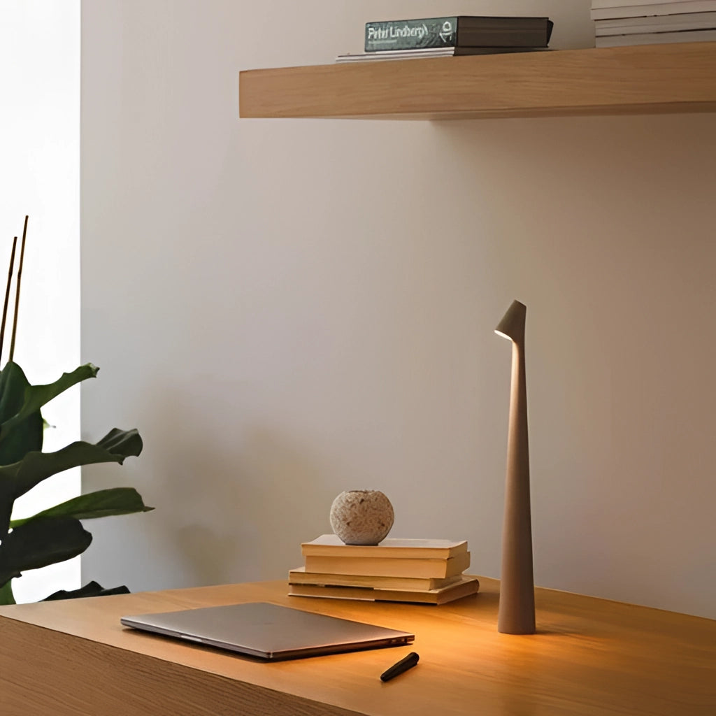 Portable rechargeable LED table lamp with aluminum construction, placed on a wooden table, next to a houseplant, in a modern interior setting.