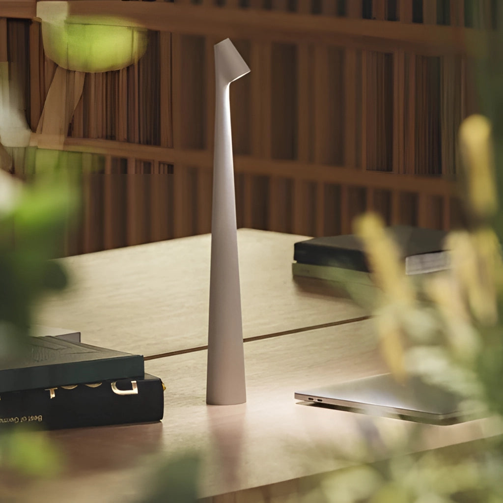 Portable rechargeable LED table lamp with aluminum construction on a wooden table next to a couch, featuring three light intensities.
