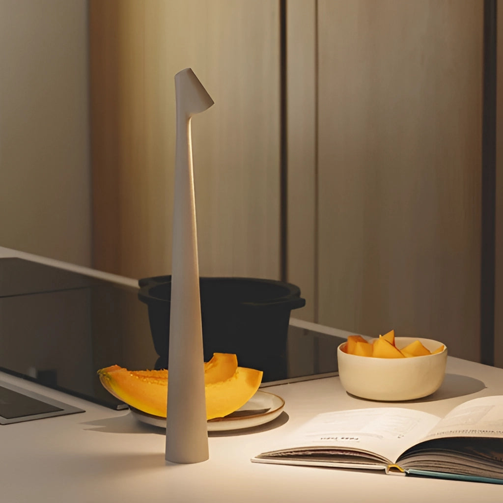 Portable rechargeable LED table lamp with aluminum construction and three light intensities placed on a wooden table next to dishware and serveware.