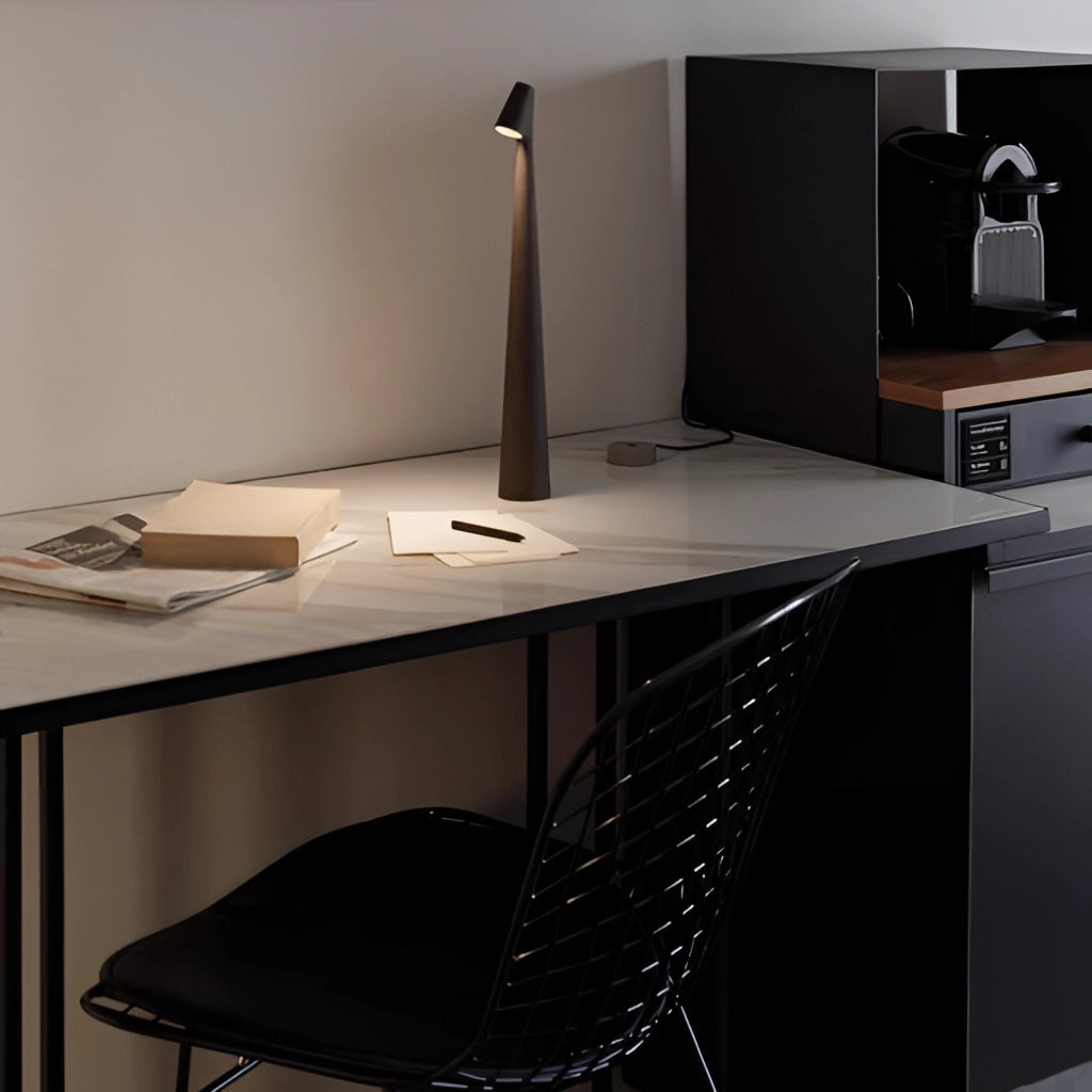 Portable rechargeable LED table lamp with aluminum construction on a wooden computer desk in a modern interior setting.