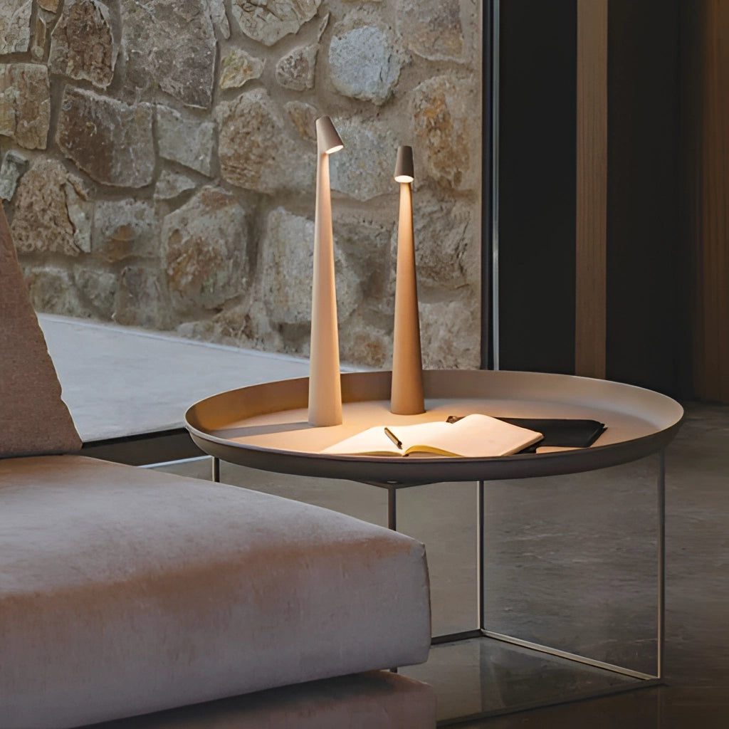 Portable rechargeable LED table lamp with aluminum construction and three light intensities placed on wooden surface in a modern interior design setting.
