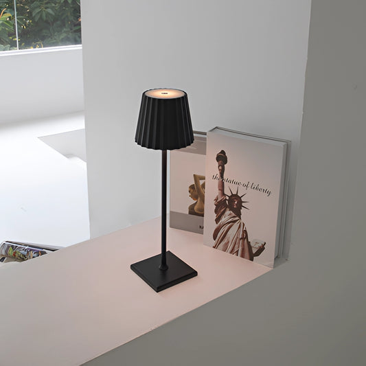 Cordless LED table lamp with stepless dimming on a wooden table, featuring a sleek grey design and modern interior decor elements in the background.