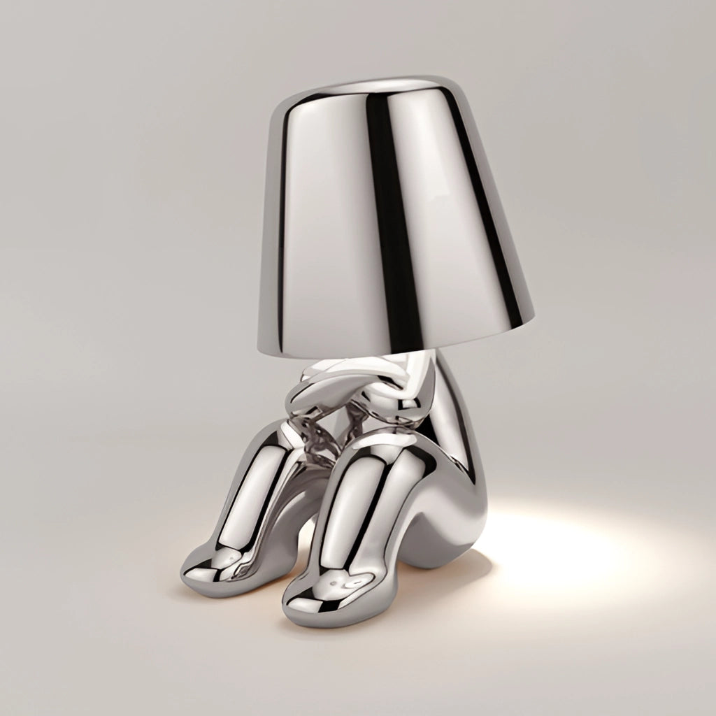 Modern gold thinker statue LED table lamp with silver accents, featuring a human leg design element.