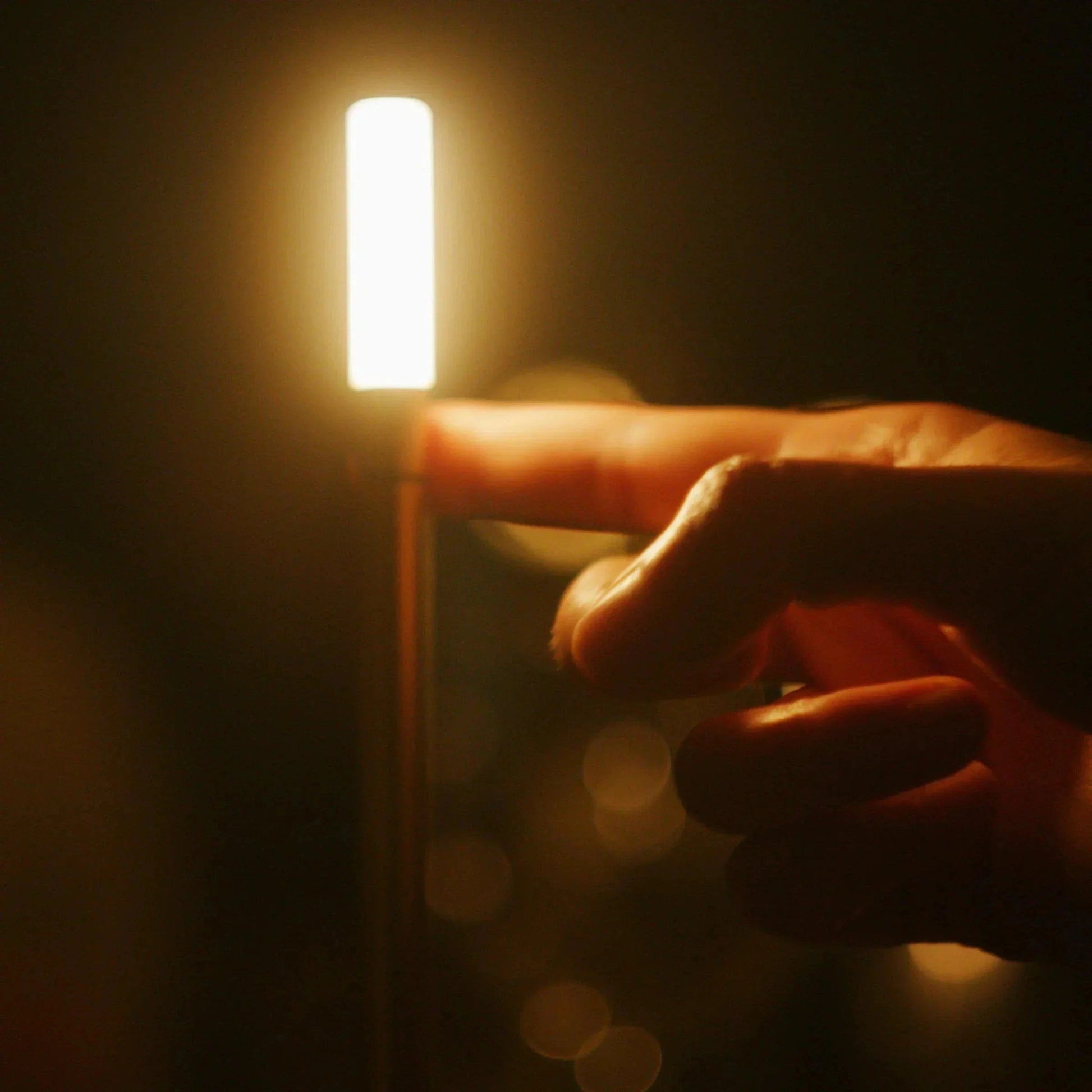 Nordic Candlestick Light with adjustable dimming and rechargeable aluminum casing, held in hand, emitting a warm amber glow in the dark.
