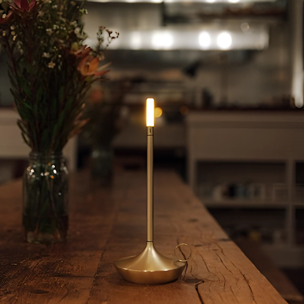 Gold Nordic Candlestick Light with adjustable dimming and rechargeable features, aluminum casing, placed on a wooden table near a vase with plants.