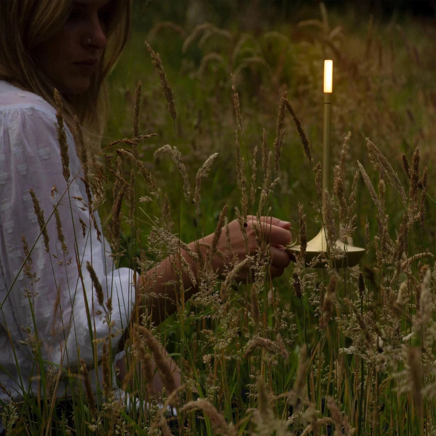 A sleek Nordic candlestick light with adjustable dimming, housed in an aluminum casing, placed on a table next to a small potted plant in a natural landscape setting.