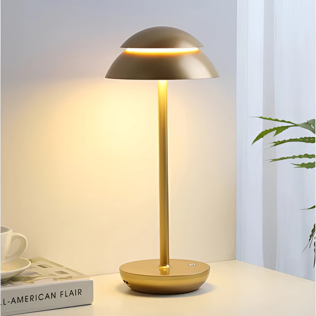 Scandinavian design table lamp in gold with a white lampshade, placed on a wooden table beside a coffee cup and plant in a modern interior setting.