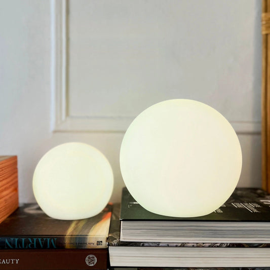 Rechargeable Cordless LED Moon Table Lamp with 16 Color Options, 6 inches, placed on a wooden table with shelving and hardwood flooring in the background.