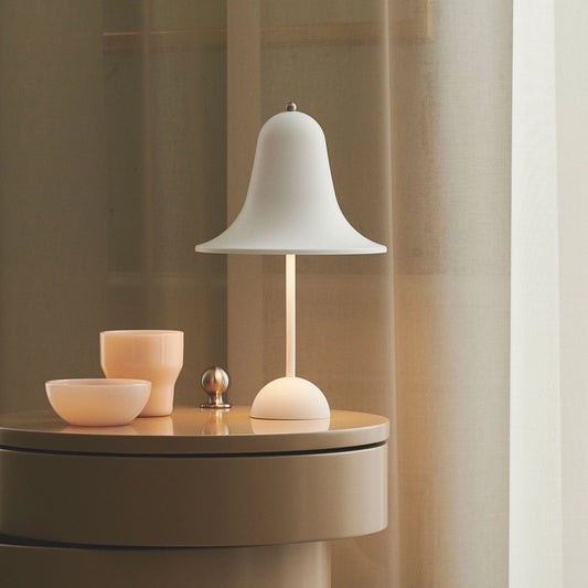 Rechargeable LED lamp with touch sensor, placed on a wooden table in a modern interior design setting, surrounded by dishware and shelving.