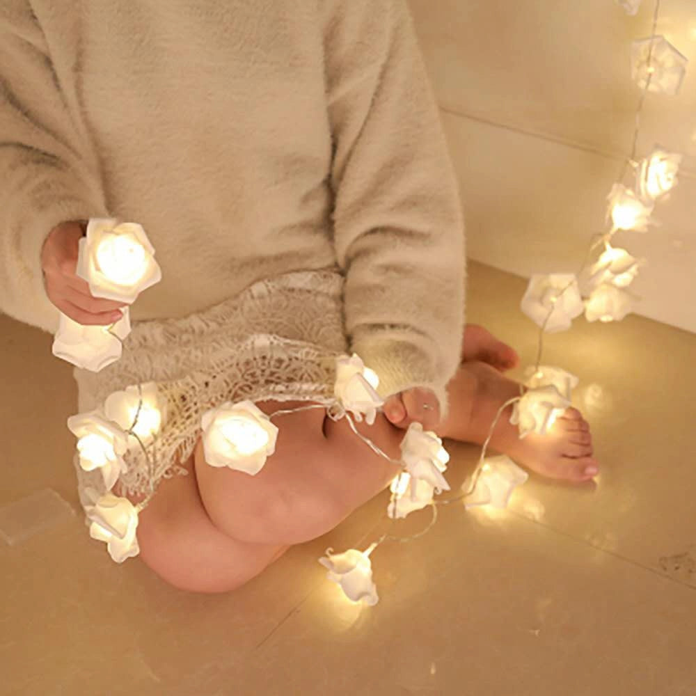 Hand holding a string of elegant rose flower LED lights on a wooden surface.