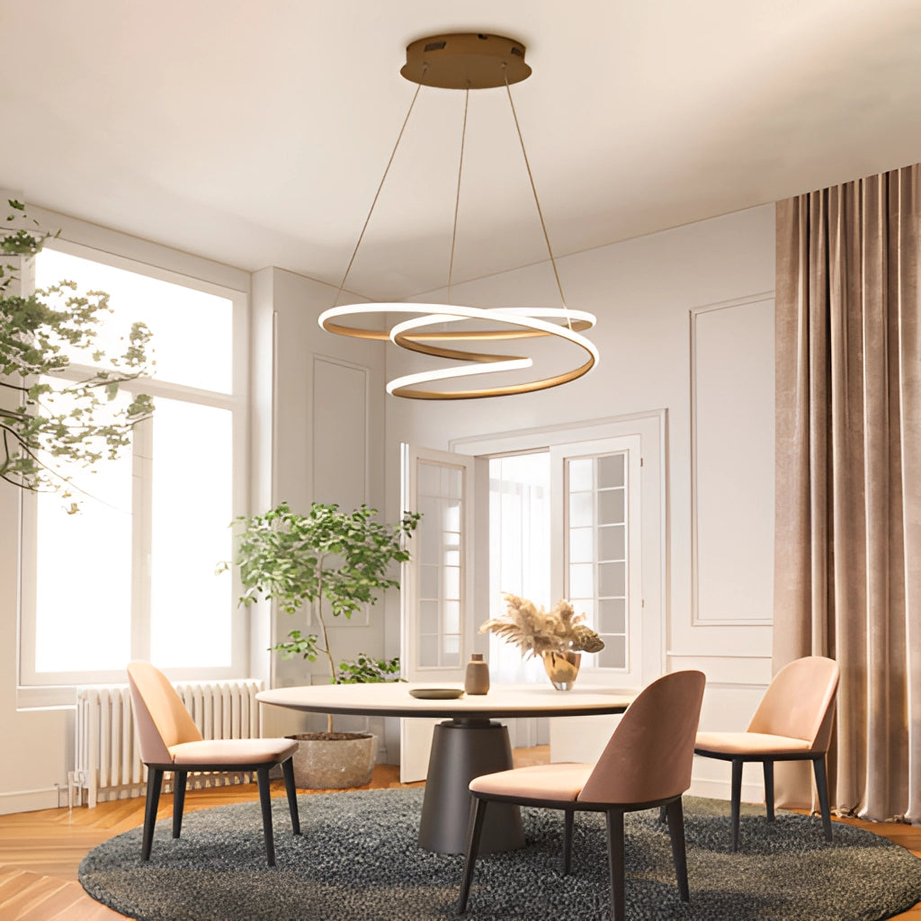 Elegant aluminum spiral pendant light with warm illumination hanging above a wooden table and chairs in a modern interior setting with plants and large windows.