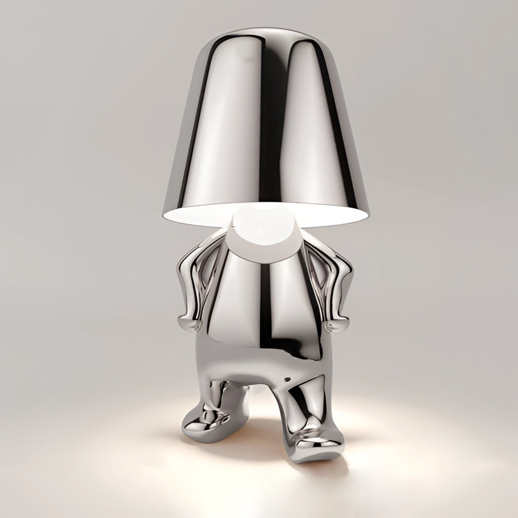 A stylish desk and nightstand lamp named Luka in silver, featuring a sleek metal design and a thinker figurine base, providing serene lighting.