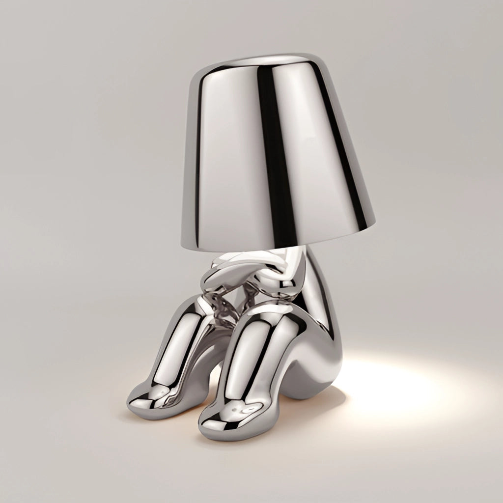 Stylish Thinker Lamp - Lasse variant in silver, placed on a desk with a modern design, featuring a sleek metal base and an elegant figure in a thinking pose as the lamp structure.