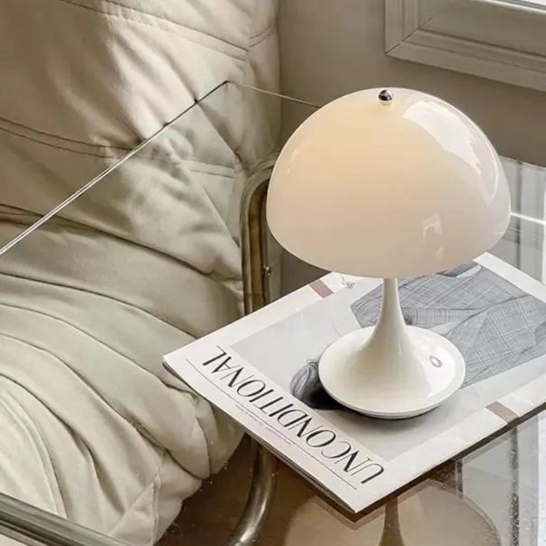 A sleek and modern Louis Poulsen Panthella 160 portable table lamp in white, black, orange, gold, and gray, with a circular shade and minimalist design, placed on a wooden table.