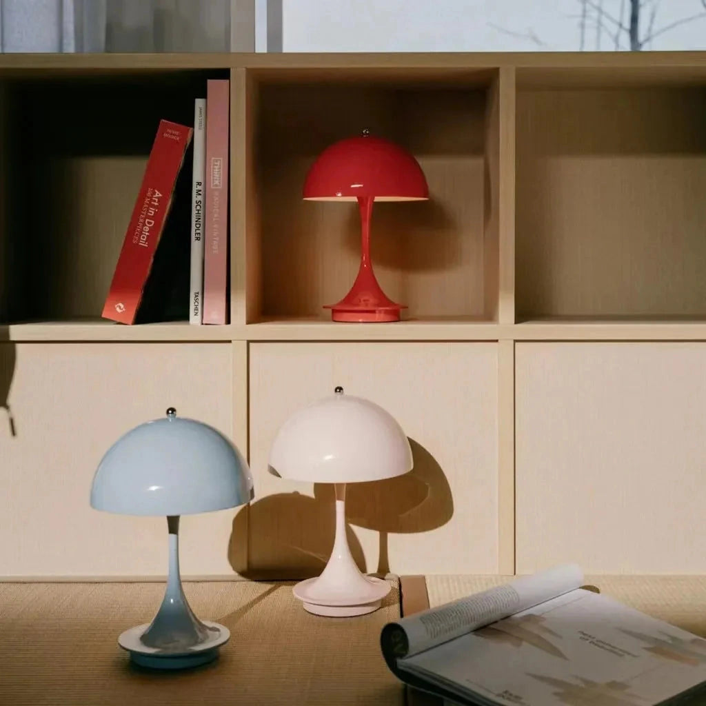Louis Poulsen Panthella 160 portable table lamp in white, black, orange, gold, and gray, placed on a wooden shelf within a stylish interior design setting.