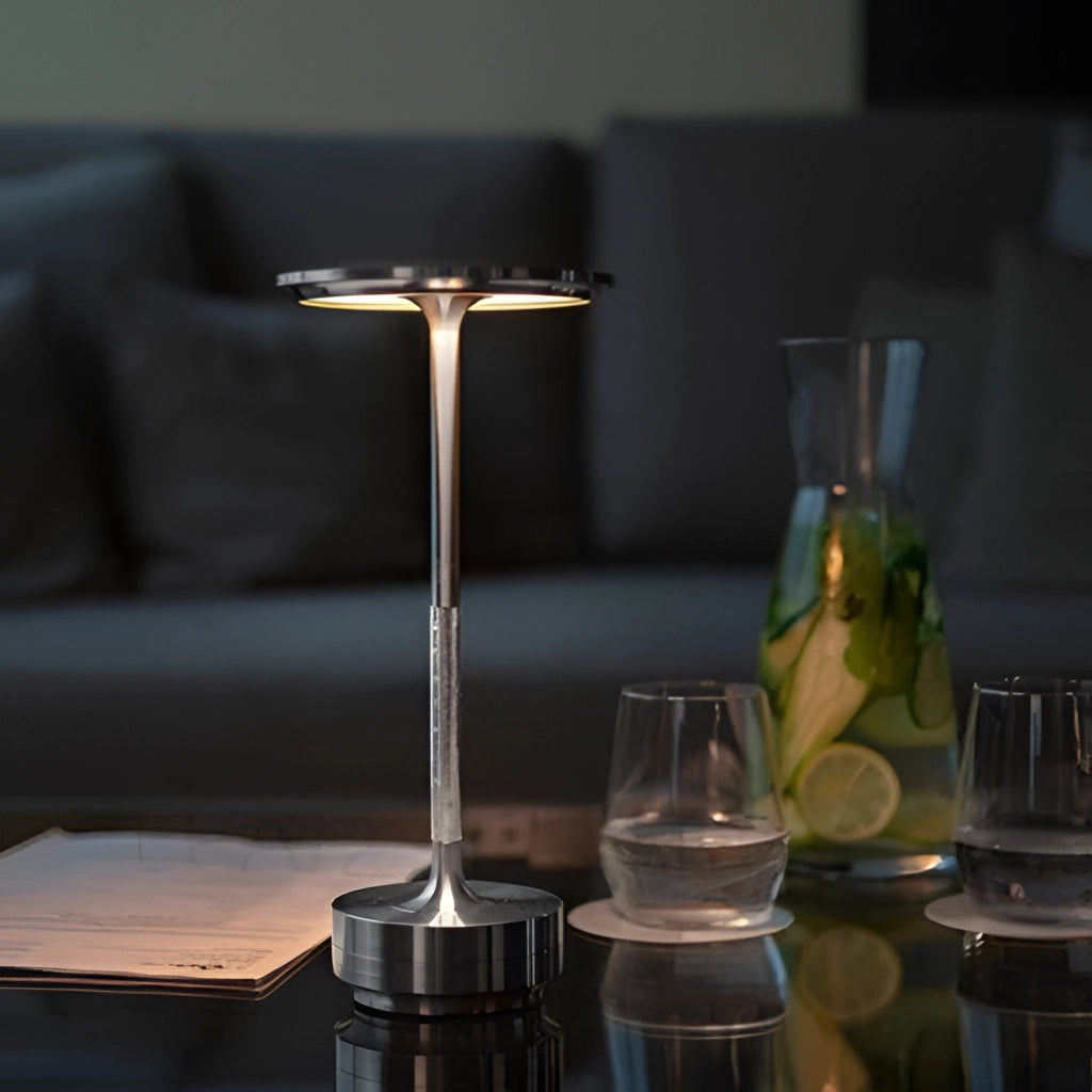 A table lamp with a sleek design and dimming feature, placed on a table surrounded by various drinkware including champagne glasses and barware.