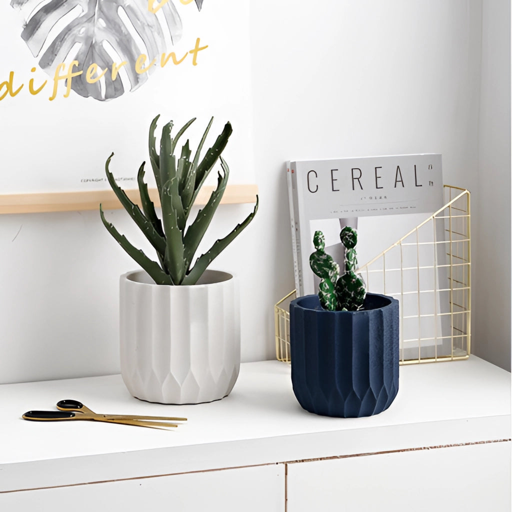 A textured ceramic polygon vase with a geometric design, placed on a table, containing a houseplant. The scene includes elements of interior design such as a couch and lighting, with a grey color scheme.