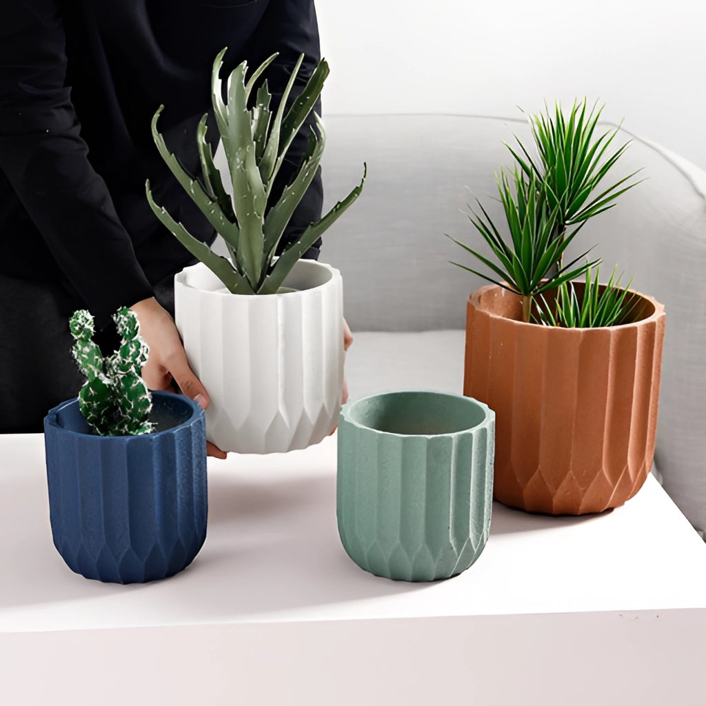 A textured ceramic polygon vase with a geometric design, containing a green houseplant, on a white background.