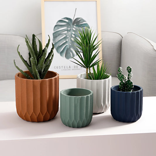 A textured ceramic polygon vase with a geometric design placed next to a green houseplant on a white flowerpot in a cozy interior setting.