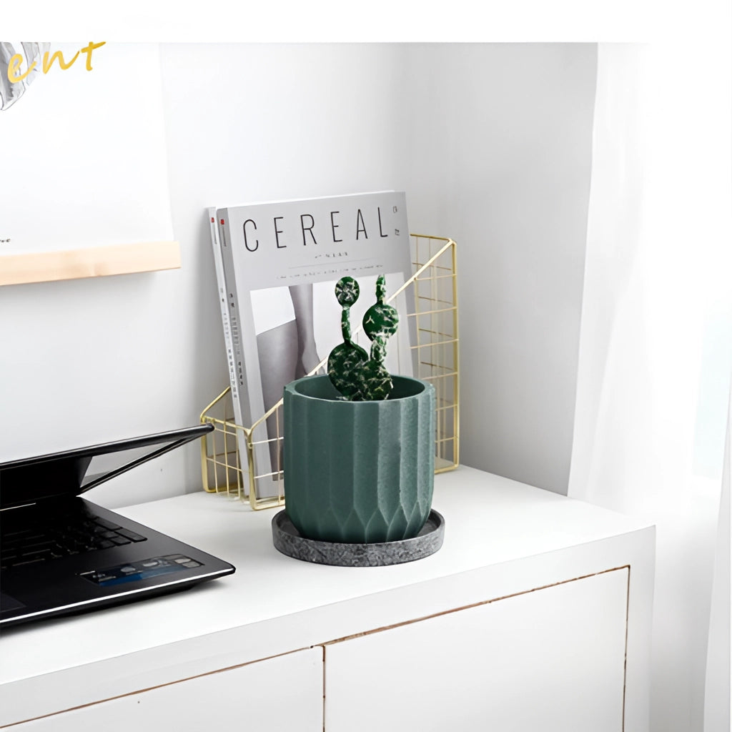 A textured ceramic polygon vase with a geometric design placed on a table next to a houseplant and a laptop.
