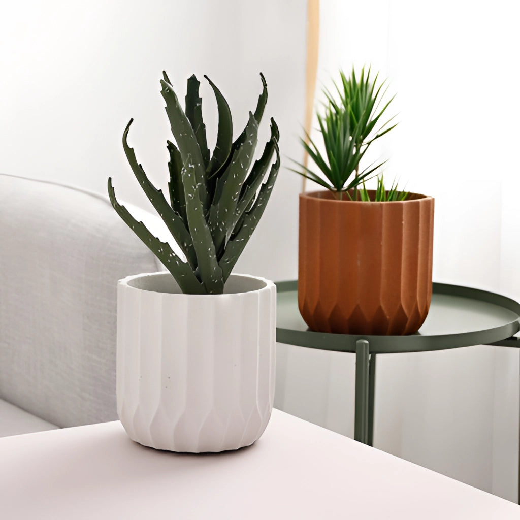 A textured ceramic polygon vase with a geometric design sits on a wooden table beside a couch, holding a vibrant houseplant.