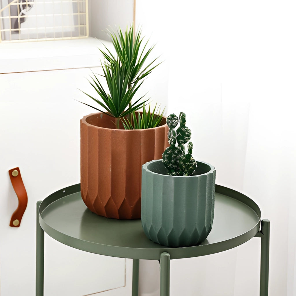 A textured ceramic polygon vase with a geometric design holding a houseplant, placed on wooden flooring near a window in a comfortable, well-furnished interior setting.
