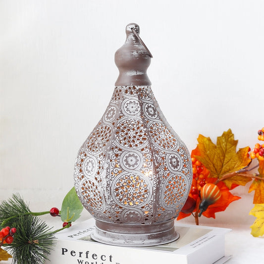 Vintage Moroccan metal lantern with intricate designs, battery-powered, placed on a table next to a potted plant and near a window.