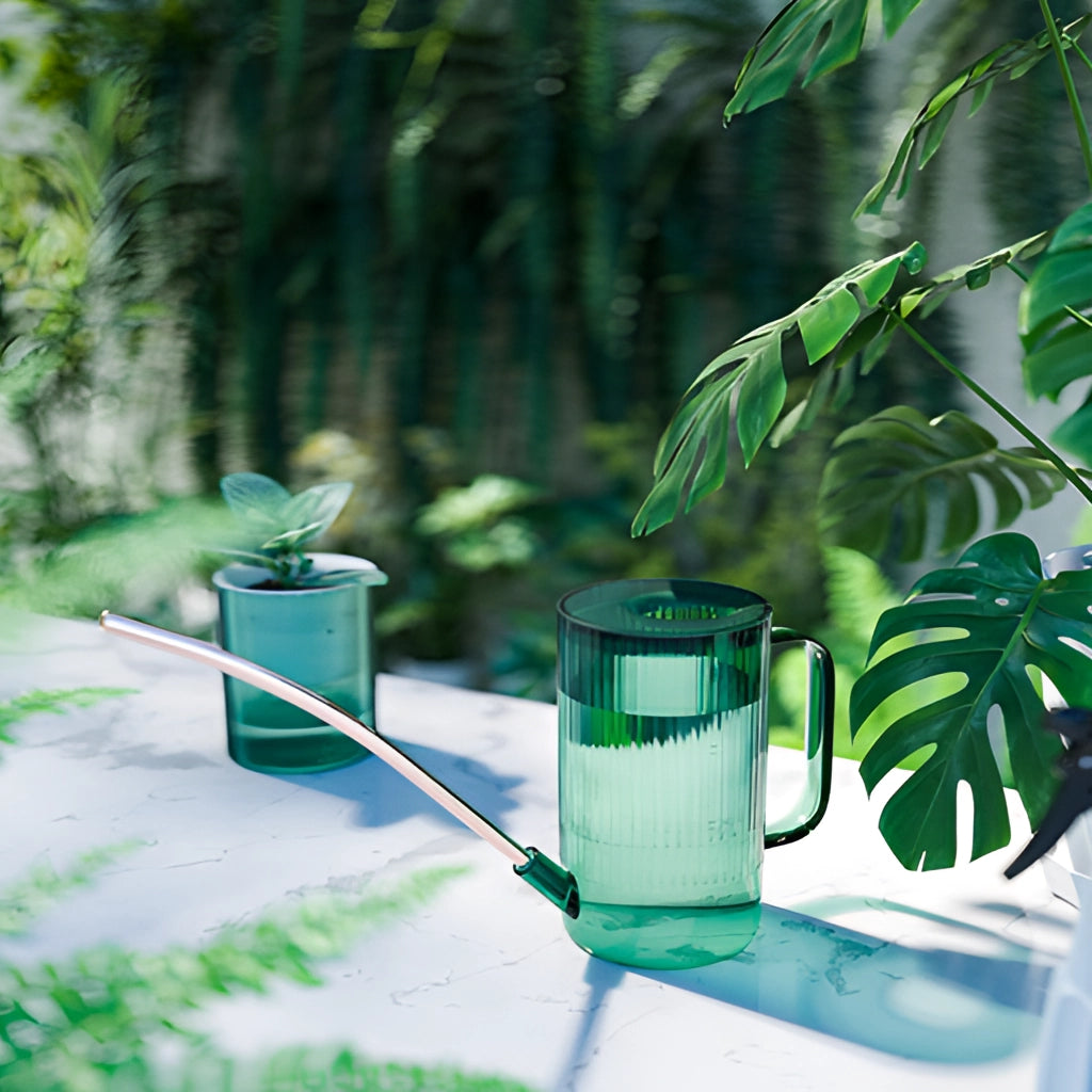 A green watering can with an extended spout for accurate water delivery, surrounded by lush green plants and bright sunlight.