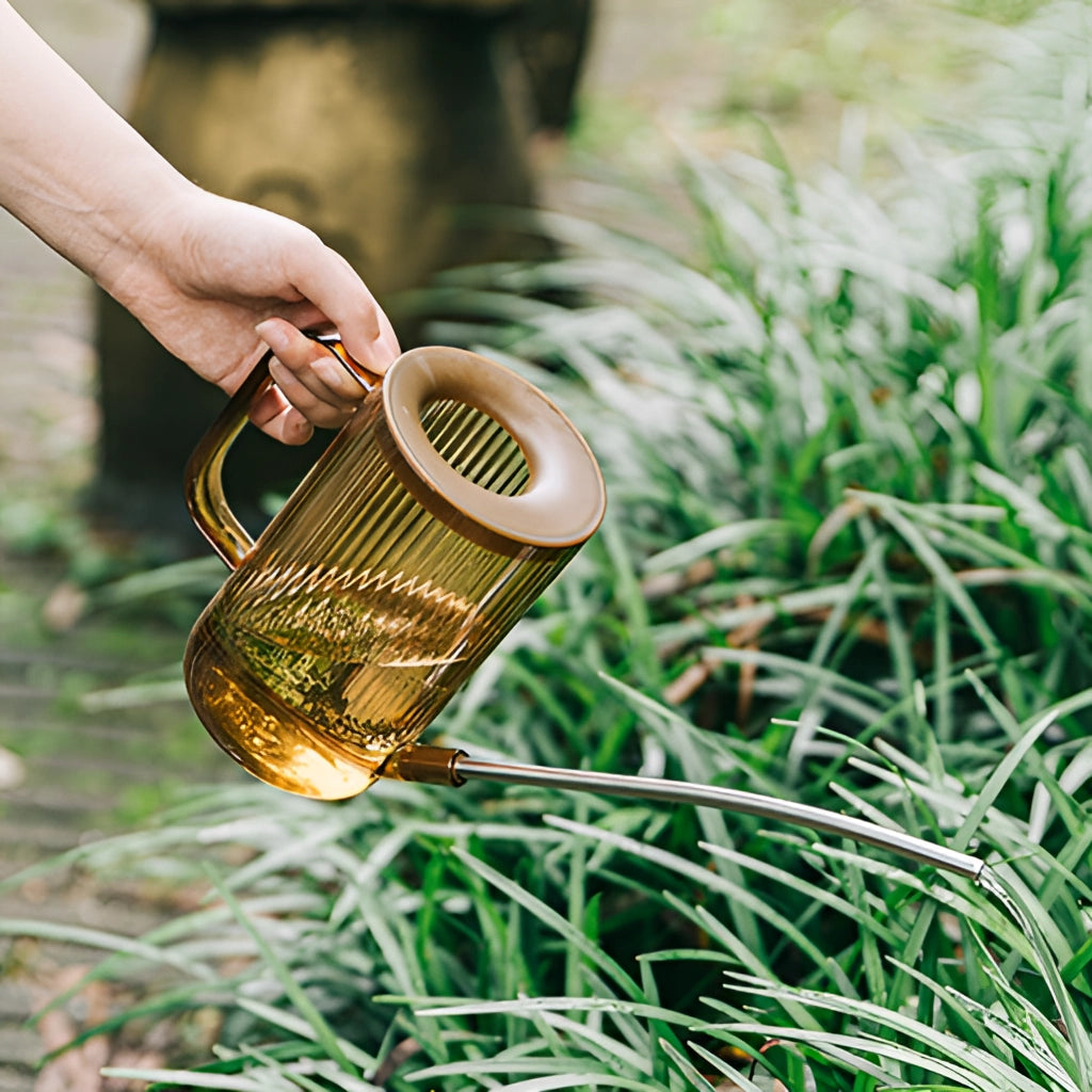 A sleek watering can with an extended spout designed for accurate water delivery, positioned next to a healthy green plant on grass.